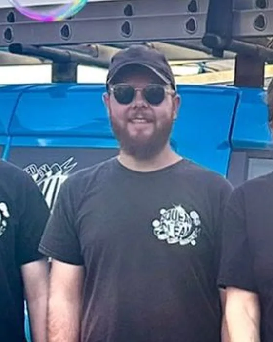James in a black Squeak-E-Clean T-shirt, cap and sunglasses, in front of the blue van