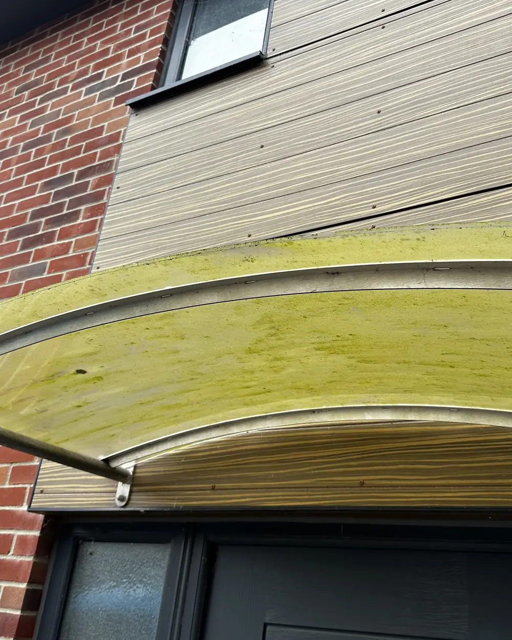 Before: a clear door canopy over a front door, stained green with algae