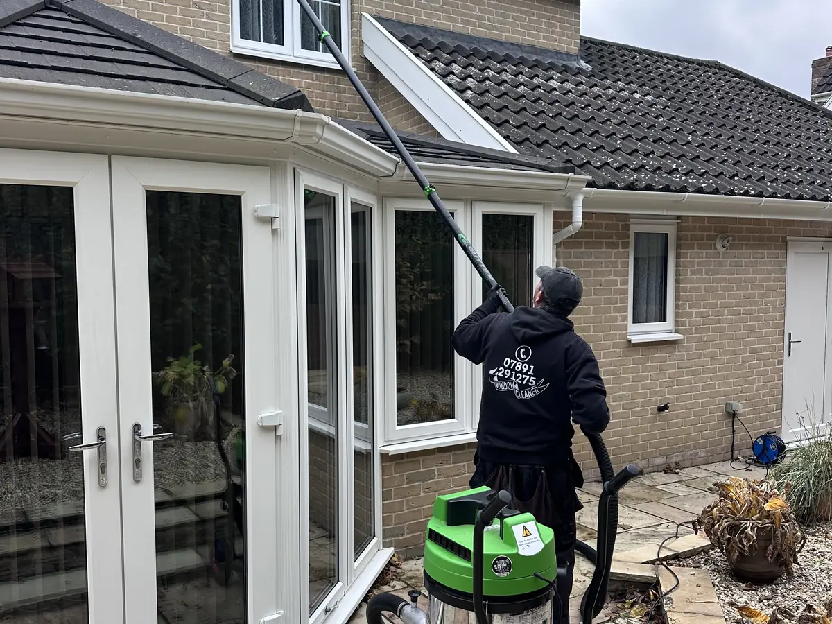 A Squeak-E-Clean cleaner on a patio clearing gutters with a green vacuum on a long pole