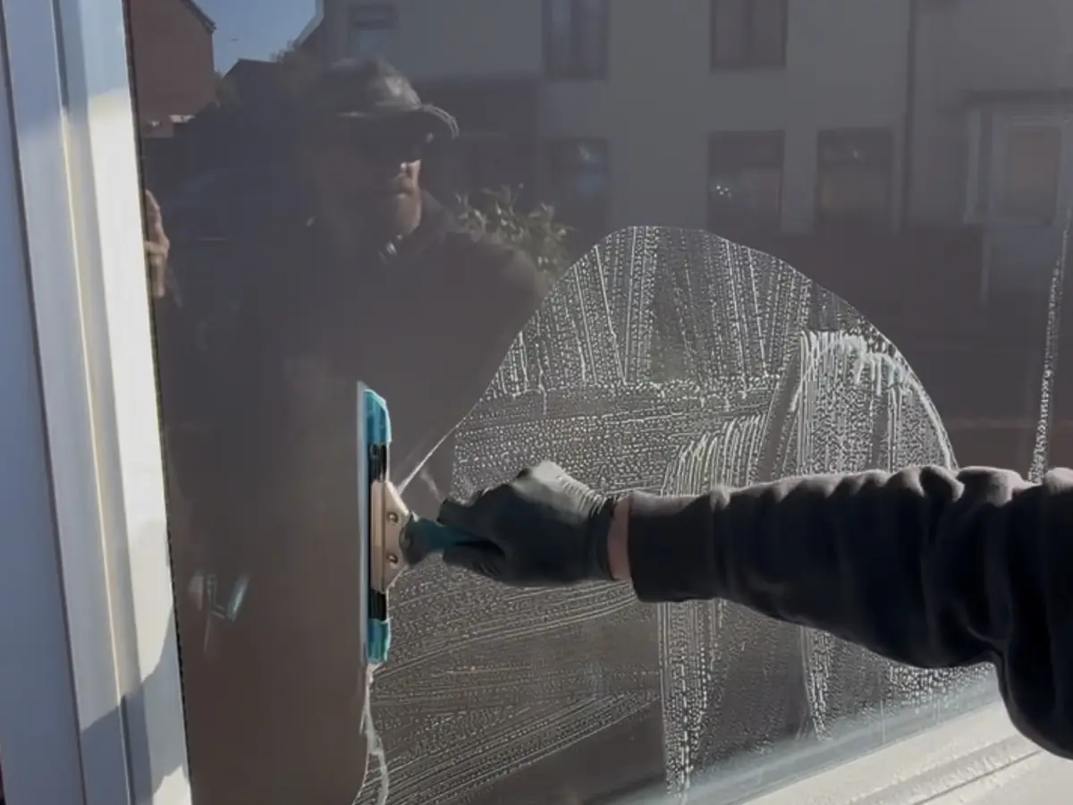 A squeegee drawn across a soapy window by hand